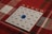 A bingo card is placed on a red and white plaid tablecloth. The card has columns labeled B, I, N, G, and O, each filled with numbers. A blue transparent marker is placed on the number 22 under the N column.