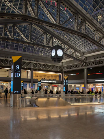 a large clock hangs from the ceiling of a large airport