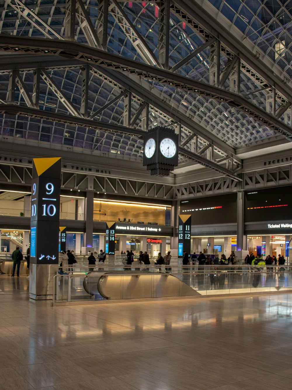 a large clock hangs from the ceiling of a large airport
