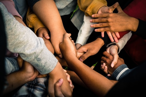 A group of diverse hands intertwined and held together, symbolizing unity and collaboration. The hands appear to belong to people of different backgrounds, conveying a powerful sense of community and support.