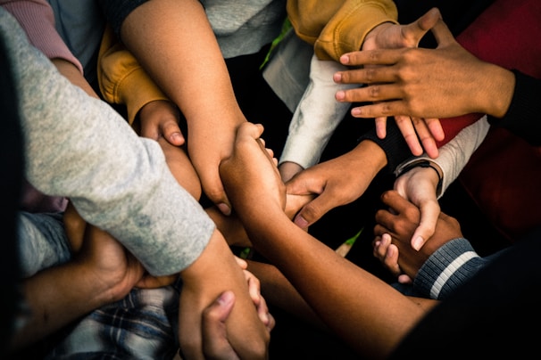 A group of diverse hands intertwined and held together, symbolizing unity and collaboration. The hands appear to belong to people of different backgrounds, conveying a powerful sense of community and support.