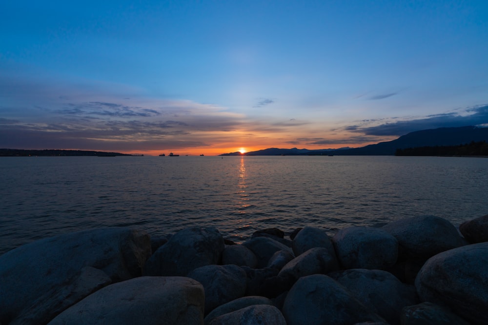 a body of water with rocks and a sunset in the background