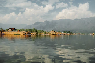 A beautifully decorated houseboat floating peacefully on Dal Lake at sunset with the Himalayas in the background.