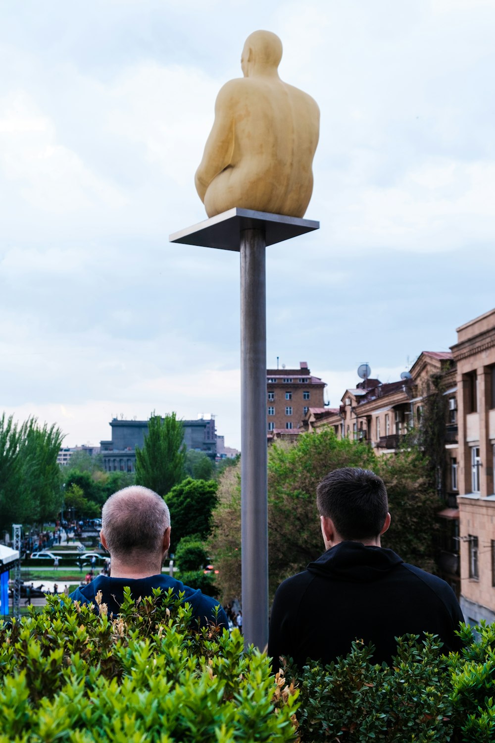 a couple of men looking at a statue of a man on a pole