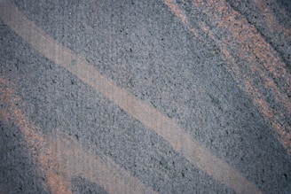 A textured surface featuring intersecting diagonal lines of dark gray and light brown. The patterns suggest a natural stone or granite material.