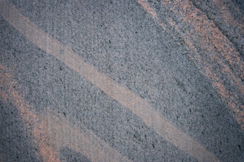 A textured surface featuring intersecting diagonal lines of dark gray and light brown. The patterns suggest a natural stone or granite material.