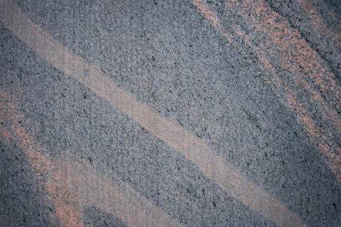 A textured surface featuring intersecting diagonal lines of dark gray and light brown. The patterns suggest a natural stone or granite material.