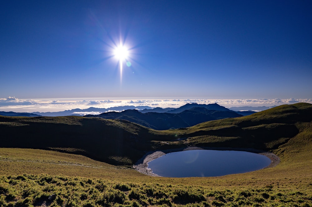 a lake surrounded by hills and a blue sky
