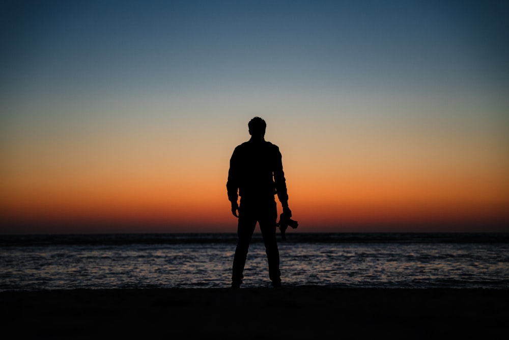 a man standing in front of a sunset over a body of water