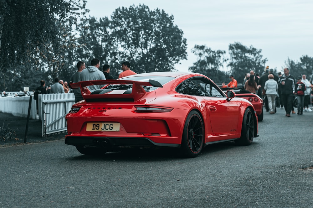 a red sports car on a road with people standing around