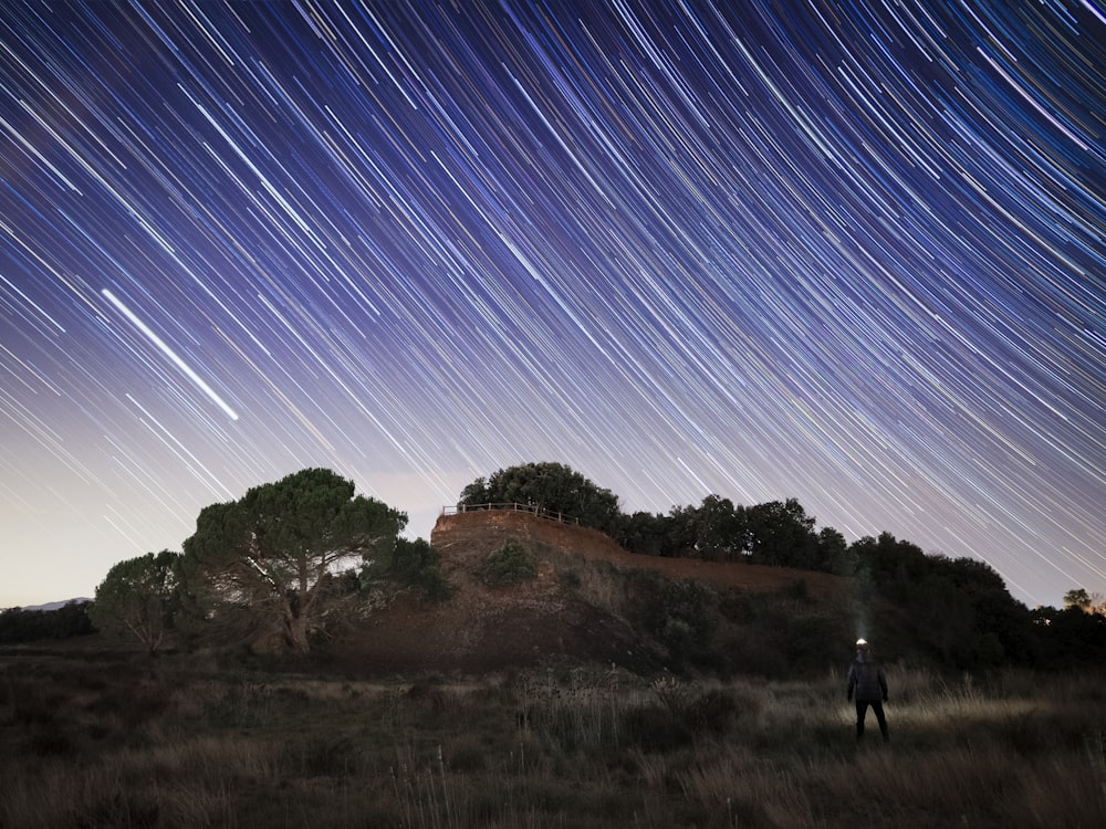 Una persona caminando sobre una colina con árboles y estrellas en el cielo