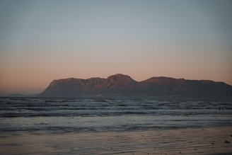 A stunning sunrise over a serene beach, capturing soft sand and calm waves with a hint of distant mountains.
