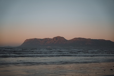 A stunning sunrise over a serene beach, capturing soft sand and calm waves with a hint of distant mountains.