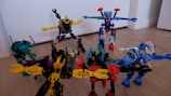 A group of colorful toy robots arranged on a wooden floor, featuring vibrant colors and intricate designs. Each robot is made of interlocking pieces in various poses, showcasing imaginative play. The scene captures a dynamic and playful moment, with toys spread out across the floor.