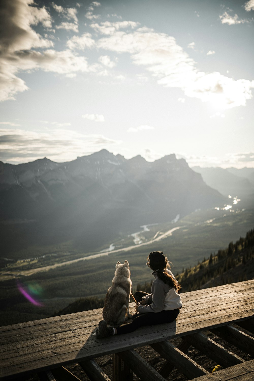 a person and a dog sitting on a wooden deck overlooking a valley