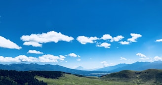 Scenic view of the Idaho mountains with rolling farmland in the foreground under a bright blue sky.
