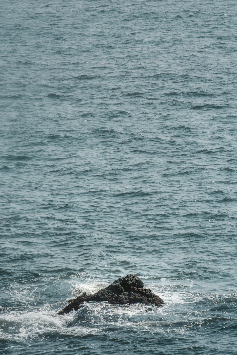 Large rock jutting out from the water's surface in the serene ocean scene