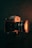 A vintage camera is prominently displayed against a dark background. The camera is metallic, with intricate dials and a large lens that emits a warm, orange glow. The lighting highlights the texture of the camera and creates a moody atmosphere.