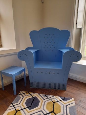A contemporary lounge area featuring a deep blue armchair, patterned rug, and rustic wooden side table.