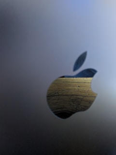 A metallic surface features a cutout in the shape of an apple with a leaf. The cutout reveals a wooden texture behind it, showcasing grain and a natural pattern.