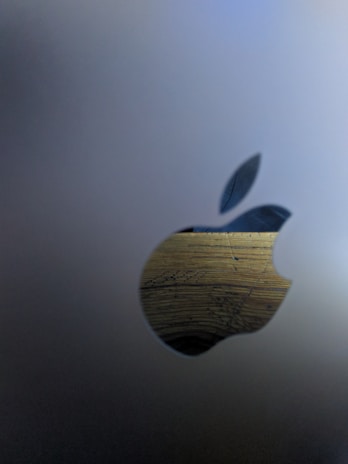 A metallic surface features a cutout in the shape of an apple with a leaf. The cutout reveals a wooden texture behind it, showcasing grain and a natural pattern.