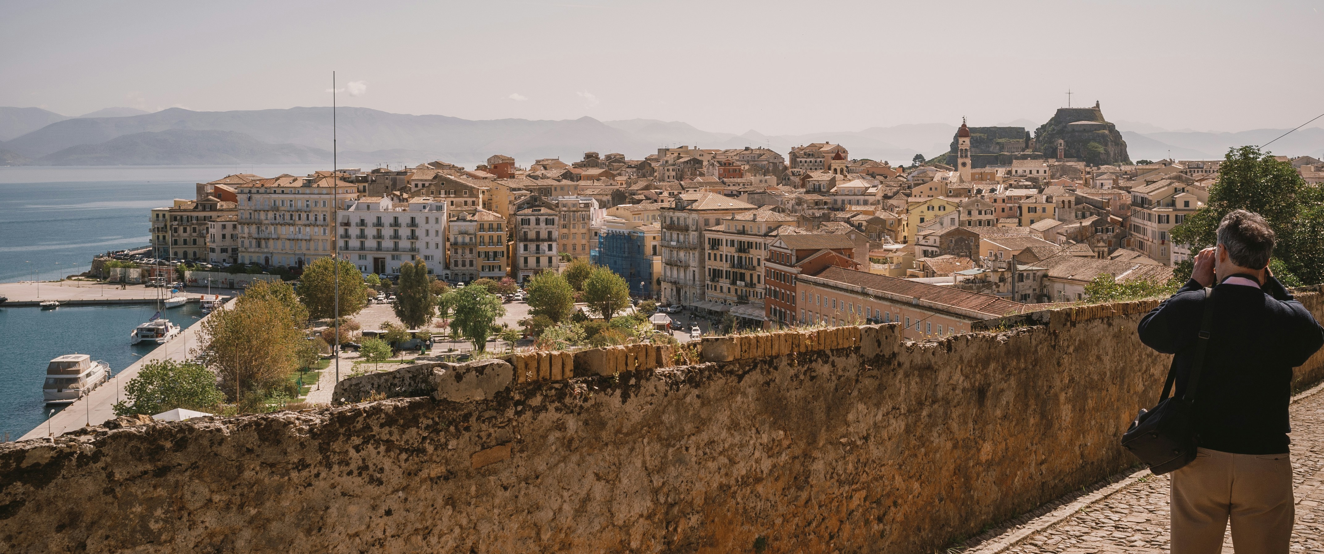 a person standing on a stone wall overlooking a city and water