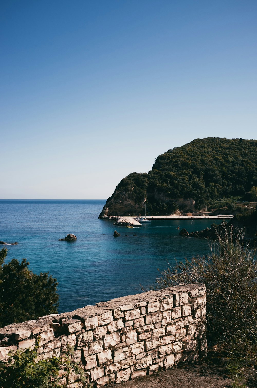 a stone wall with a body of water and a hill with trees