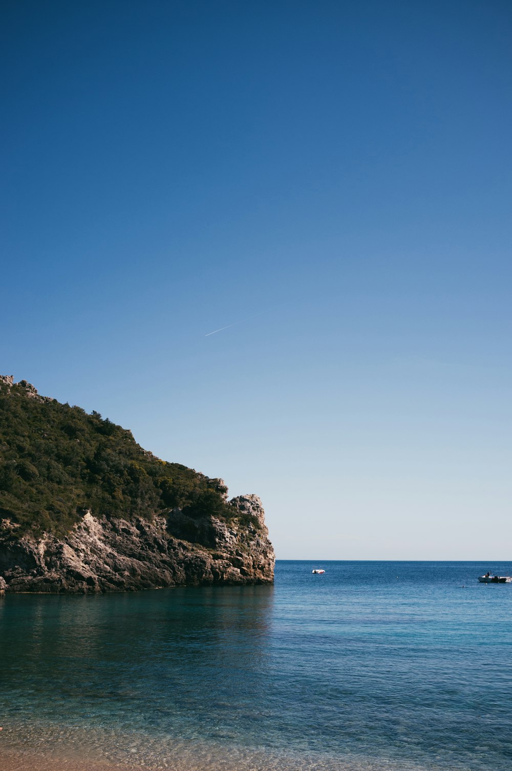 a body of water with a rocky cliff and a beach with boats