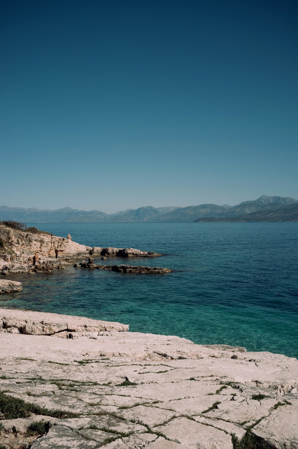 a rocky beach with a body of water and mountains in the background