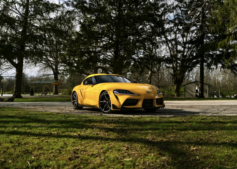 a yellow sports car parked on a road with trees and grass