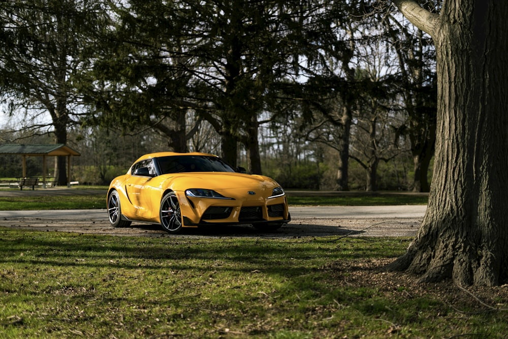 a yellow sports car parked on a road with trees and grass