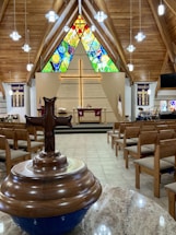A warm, inviting church sanctuary with a cross and congregation watching a live stream on a large screen