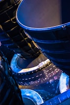 A close-up view of intricate metallic machinery showcasing curved components and structural panels. Bright illumination highlights the textures and details of the surfaces, with a distinct blue and gold color theme giving a futuristic and industrial aesthetic.