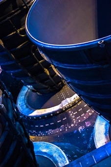 A close-up view of intricate metallic machinery showcasing curved components and structural panels. Bright illumination highlights the textures and details of the surfaces, with a distinct blue and gold color theme giving a futuristic and industrial aesthetic.