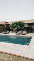 Side view of a concrete pool with a wooden deck and minimalist outdoor furniture.
