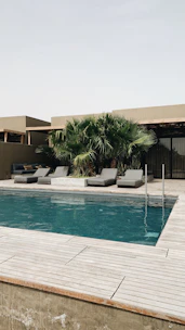 A sleek backless bench placed beside a sparkling pool under clear skies.