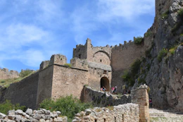 a stone building with a stone wall and people walking around