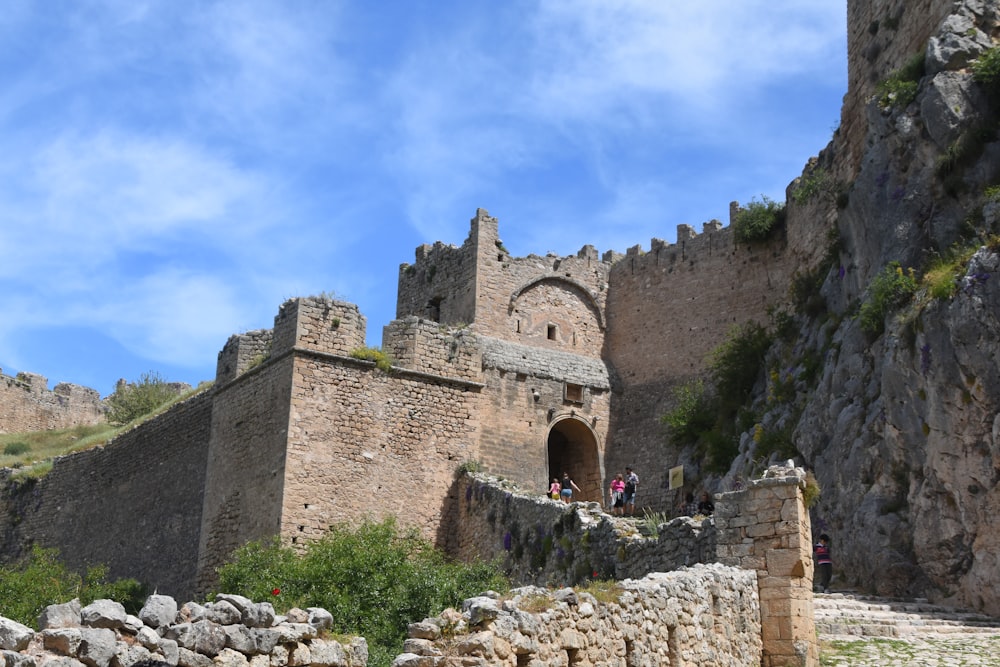 a stone building with a stone wall and people walking around