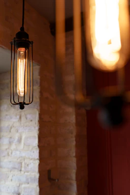 Close-up of a glowing industrial cage light hanging against a rustic brick wall