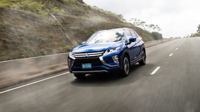 Side view of a blue SUV driving along a scenic road with mountains in the background.