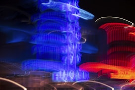 Neon lights create an abstract scene with intense blue and red hues against a dark background. The light trails appear to be from signs or buildings, forming swirling patterns.
