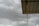 A corrugated metal roof supported by a vertical metal beam, set against a backdrop of overcast, cloudy skies. The sky appears dark grey, suggesting an approaching storm or rain.