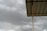 A corrugated metal roof supported by a vertical metal beam, set against a backdrop of overcast, cloudy skies. The sky appears dark grey, suggesting an approaching storm or rain.