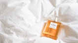 A bottle of Chanel No. 5 perfume rests on a soft, white quilt, highlighting its elegant design and golden liquid.
