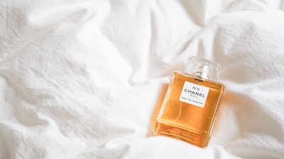 A bottle of Chanel No. 5 perfume rests on a soft, white quilt, highlighting its elegant design and golden liquid.
