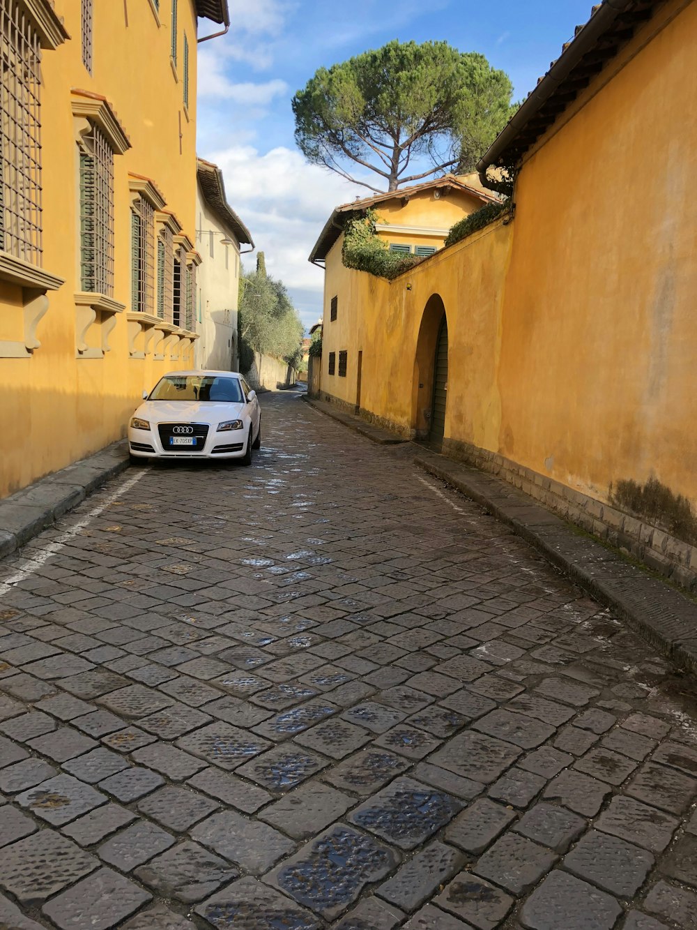 a car parked on a cobblestone street between buildings