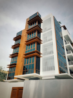 A modern multi-story building with a combination of wooden panels and large glass windows. The structure features angular balconies and a mix of textures with vertical white slats on one segment.