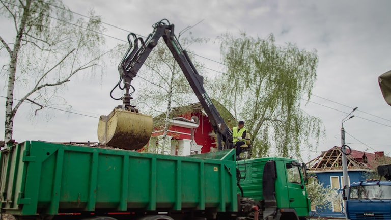 A team member from Kiwi Clean and Haul LLC carefully loading debris into a truck on a sunny day.