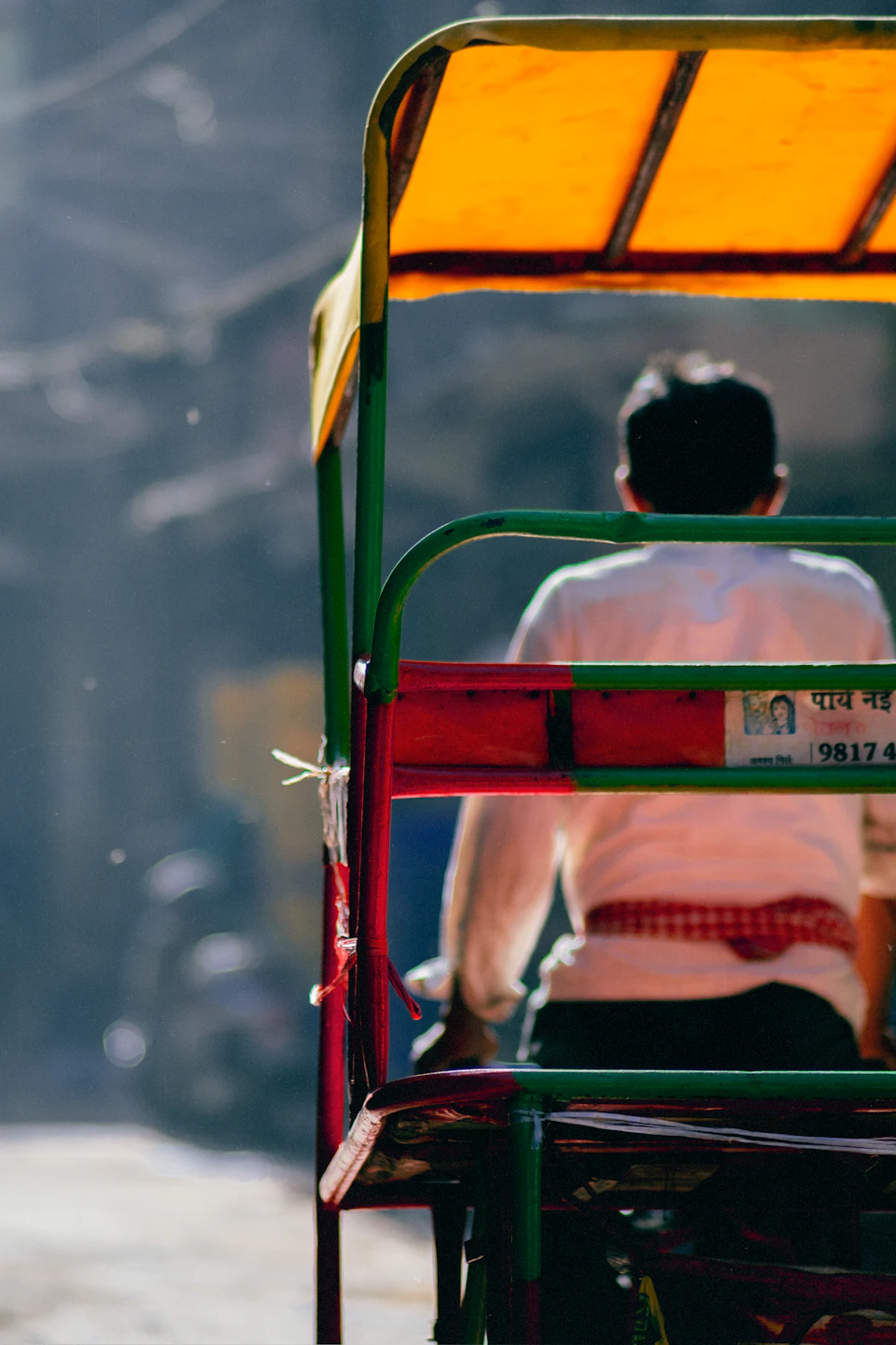 Man seated on vibrant red and green tuk-tuk parked on city street