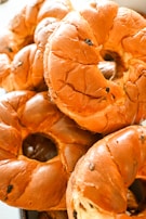 A close-up view of several freshly baked bagels, showcasing their golden-brown crusts and circular shape. The bagels have a glossy texture, with small spots indicating the presence of raisins or another similar ingredient.